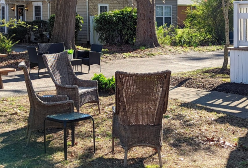 A cozy outdoor seating area with wicker chairs and a small table, surrounded by greenery and pathways.