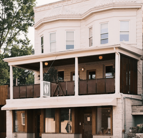 A charming two-story building with a porch, large windows, and a welcoming entrance, surrounded by trees.