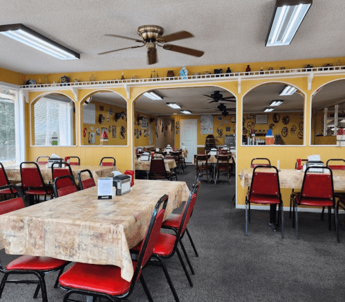 Cozy diner interior with red chairs, tables covered in patterned cloth, and yellow walls adorned with decor.