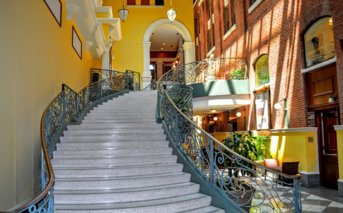 A grand staircase with ornate railings, surrounded by yellow walls and large windows, in a well-lit interior space.