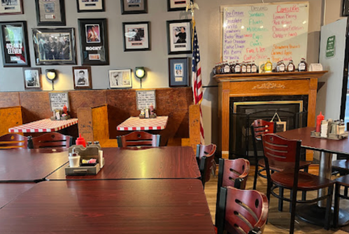 Cozy restaurant interior with wooden tables, red and white checkered tablecloths, and a fireplace adorned with photos.