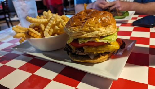 A juicy cheeseburger with lettuce, tomato, and onion, served with a side of crispy fries on a checkered table.
