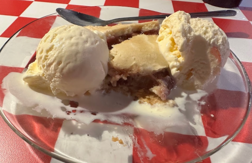 A slice of pie topped with two scoops of vanilla ice cream, served on a glass plate with a spoon.