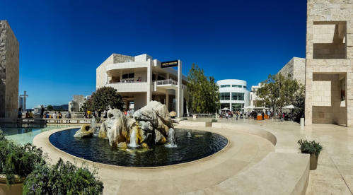 A sunny outdoor view of a modern museum complex with a fountain and people enjoying the space.