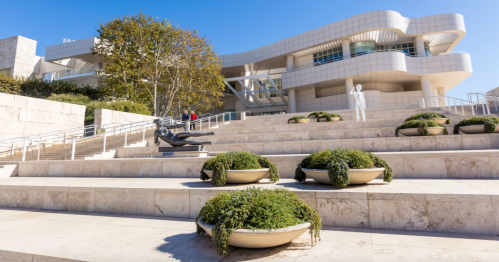 A modern building with a unique design, surrounded by landscaped steps and planters, under a clear blue sky.