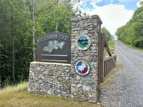 Sign for Big Canoe Creek Nature Preserve with stone structure and road leading into a wooded area.