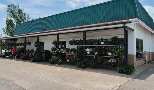 A garden center with a green roof, displaying vibrant flowers and plants along the exterior.