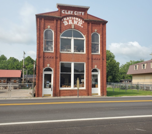 Historic red brick building with large windows, labeled "Clay City National Bank," set along a quiet road.