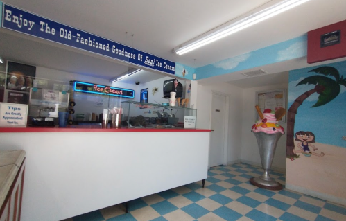 A colorful ice cream shop interior with a service counter, vibrant decor, and a large ice cream cone statue.