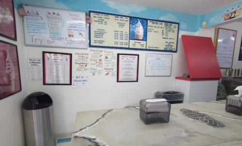 Interior of an ice cream shop featuring a menu board, specials, and a countertop with a trash can in the background.