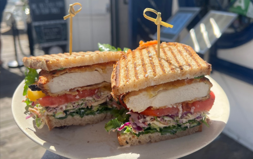 A grilled sandwich with layers of chicken, lettuce, tomato, and slaw, served on a plate with toothpicks.