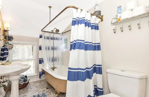 A cozy bathroom featuring a clawfoot tub, striped shower curtain, and vintage decor with a window for natural light.
