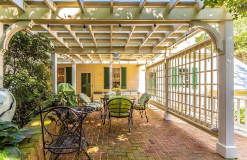 A cozy outdoor patio with a pergola, featuring a dining table and chairs surrounded by greenery.