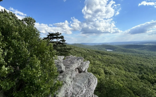 A scenic view from a rocky outcrop overlooking lush green hills and a blue sky with scattered clouds.