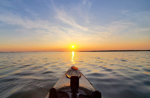 A kayak on calm water at sunset, with the sun reflecting on the surface and a colorful sky in the background.