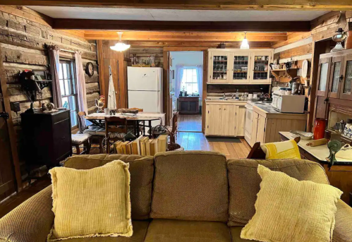 Cozy rustic kitchen and dining area with wooden walls, a sofa in the foreground, and a warm, inviting atmosphere.