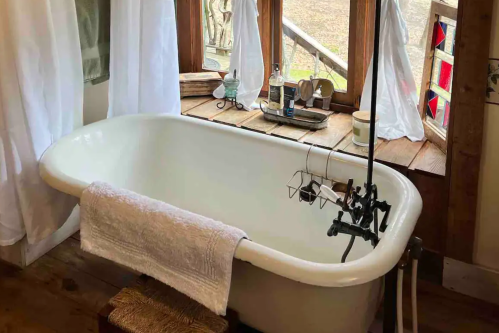 A vintage bathtub with a towel draped over it, set near a window with rustic decor and natural light.