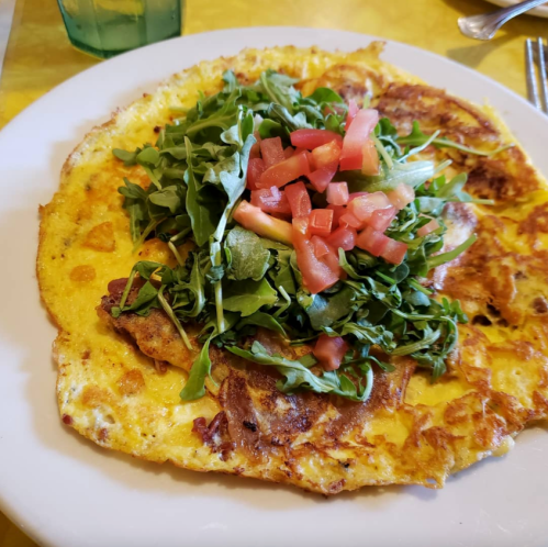 A large omelette topped with fresh arugula and diced tomatoes, served on a white plate.