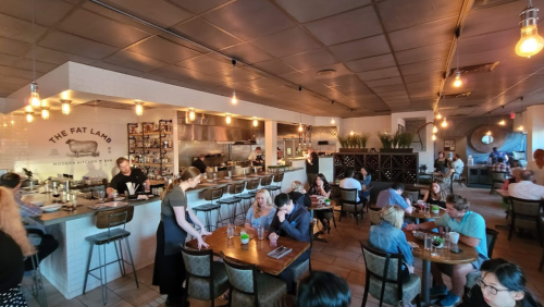 A lively restaurant interior with patrons dining, a bar area, and warm lighting, creating a cozy atmosphere.