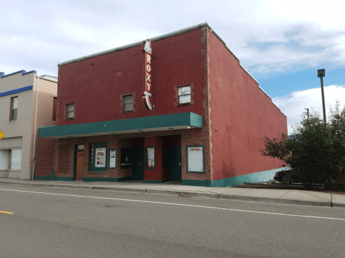 A red and teal building with a marquee sign reading "Roxy," located on a street with a cloudy sky above.