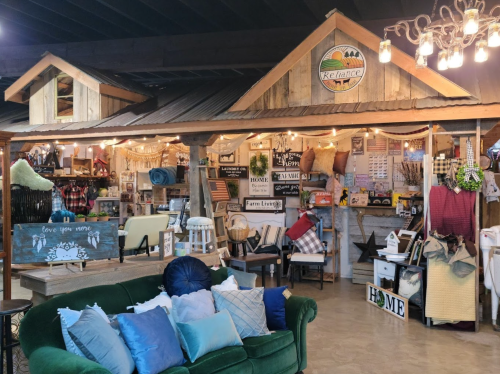 A cozy shop interior featuring rustic decor, furniture, and home goods, with a green couch in the foreground.
