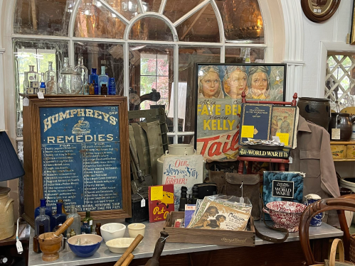 A collection of vintage items, including bottles, posters, and books, displayed in a charming antique shop.