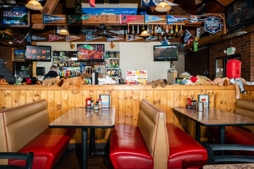 A cozy restaurant interior with wooden walls, red booths, and a bar displaying various memorabilia and stuffed animals.