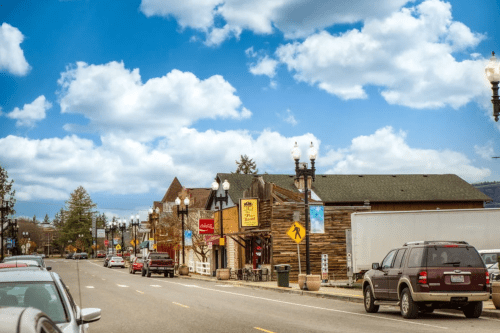 A charming street scene with shops, parked cars, and a blue sky dotted with clouds.