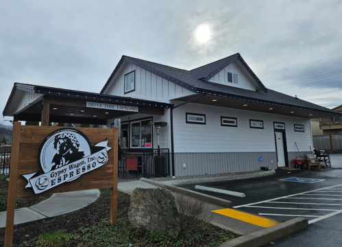 A modern drive-thru espresso shop with a wooden sign, located in a cloudy setting.