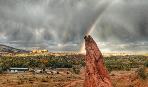 A rocky landscape under a cloudy sky, featuring a vibrant rainbow arching over the horizon.