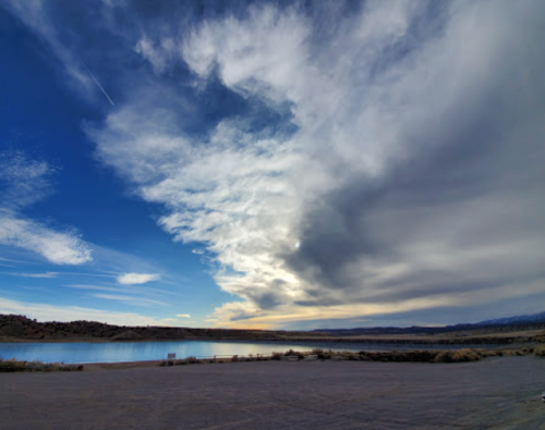 A serene landscape featuring a lake, rolling hills, and a dramatic sky with clouds at sunset.