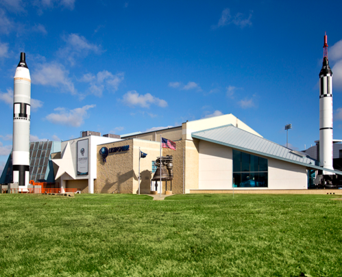 Exterior view of a space museum featuring rocket displays and a grassy area under a clear blue sky.