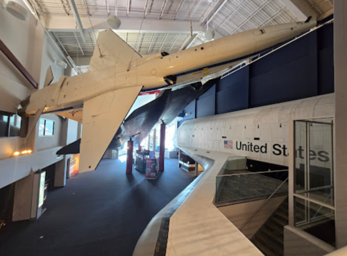 A large aircraft suspended in a museum, with a space shuttle display and "United States" signage in the background.
