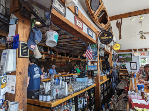 A lively bar scene with patrons at the counter, various drinks displayed, and decor featuring sports memorabilia.