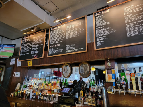 A bar with a menu on the wall, showcasing various drinks and draft beers, with a TV displaying a sports game.