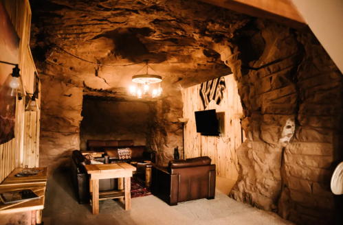 Cozy cave-like interior with leather sofas, wooden accents, and a chandelier, creating a rustic, warm atmosphere.