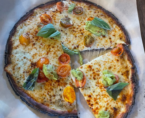 A freshly baked pizza topped with melted cheese, colorful tomatoes, and fresh basil, with one slice removed.