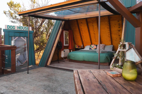 Cozy interior of a unique cabin with a bed, wooden accents, and a view, alongside a small dog house outside.