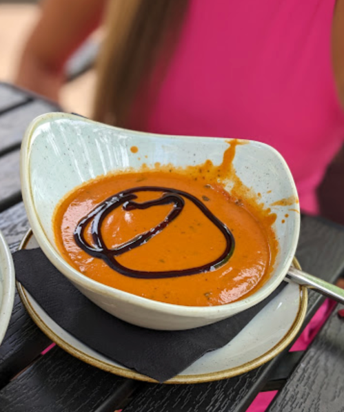 A bowl of tomato soup drizzled with balsamic glaze, served on a black napkin on a wooden table.