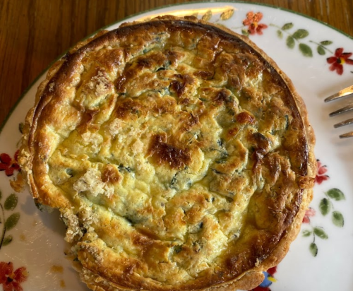 A golden-brown quiche on a floral-patterned plate, with a fork beside it.