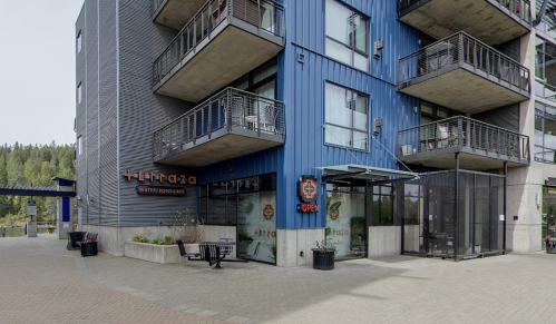 Modern building exterior with blue panels, balconies, and a sign for "Terraza Waterfront Café." Pathway in front.