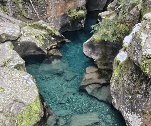 A serene, clear blue pool surrounded by moss-covered rocks and steep canyon walls.