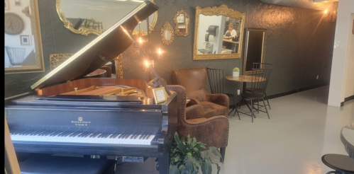 A stylish interior featuring a grand piano, cozy seating, and decorative mirrors on a dark wall.