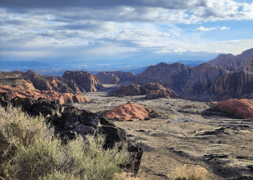 A panoramic view of rugged, colorful rock formations and a vast valley under a cloudy sky.