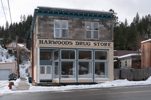 Historic Harwood's Drug Store building with large windows, snow-covered ground, and trees in the background.
