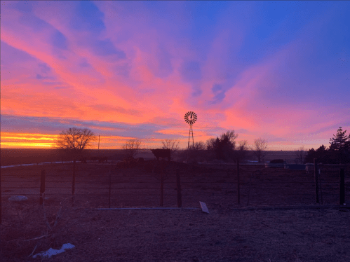 A vibrant sunset with pink and purple hues, featuring a windmill silhouette and a rural landscape.