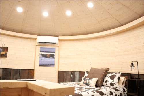 Cozy circular room with wooden walls, a bed with cow-print pillows, and modern lighting.