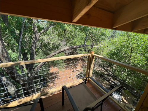 View from a wooden balcony overlooking lush greenery and trees, with two chairs positioned on the deck.