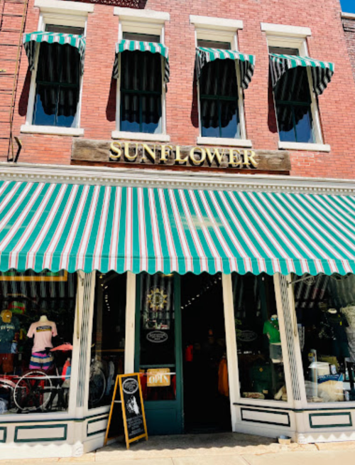 A storefront with green and white striped awnings, featuring the sign "SUNFLOWER" and an open sign in the window.