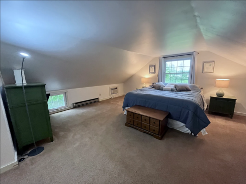 Cozy attic bedroom with a sloped ceiling, a bed, nightstands, and a window letting in natural light.